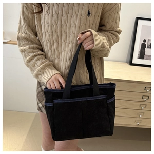 Detail view of black corduroy tote bag with blue trim pockets held by model