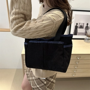 Minimalist black corduroy tote bag with side pockets shown in a cozy home setting