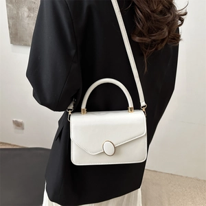 Borsa a tracolla in pelle bianca minimalista con dettagli dorati su un blazer nero elegante