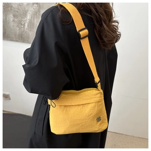 Close-up of a yellow nylon crossbody bag with metallic flower logo worn over a black coat