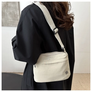 Detail of beige nylon crossbody bag with double zippers and metal flower logo