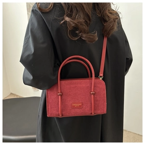 Detail of red corduroy handbag showing textured fabric and leather logo tag on shoulder