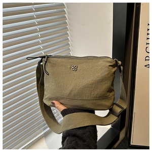 Detailed shot of an olive green nylon crossbody bag featuring a clover metal logo accent