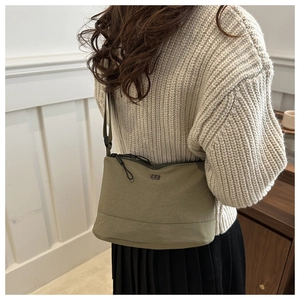 Olive green nylon crossbody bag detail with silver metal logo on model in casual knitwear