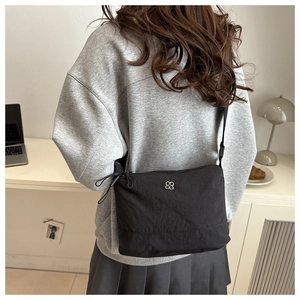 Detail of a black nylon crossbody bag with silver hardware on a casual model outfit