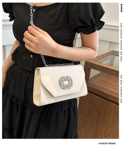 Detail of cream leather crossbody bag featuring a crystal buckle and silver chain strap