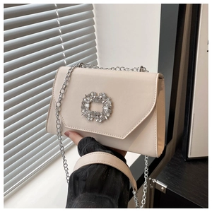 Detail of a creamy white structured shoulder bag with a square rhinestone buckle and chain