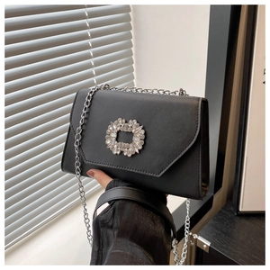 Detail of a black crossbody bag with a sparkling oversized crystal buckle and silver chain