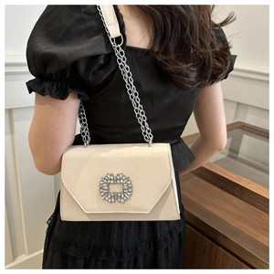 Detail of cream leather crossbody bag with a large rhinestone buckle and silver chain strap