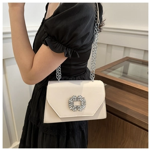 Detail of a chic cream crossbody bag with silver chain strap and sparkling rhinestone buckle