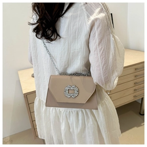Detail of beige PU leather crossbody bag with sparkling rhinestone buckle and silver chain strap