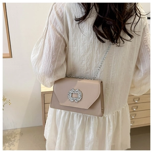 Detail of elegant beige chain bag with oversized round crystal buckle on woman's shoulder