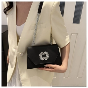Detail of a black leather crossbody bag with a sparkling rhinestone buckle and chain strap