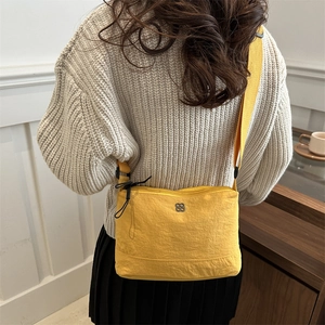 Vibrant yellow crossbody bag with metal flower logo and wide knit strap on casual outfit