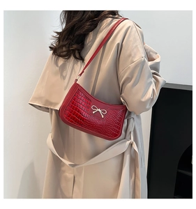 Detail of red baguette bag with crocodile texture and gold bow buckle on model