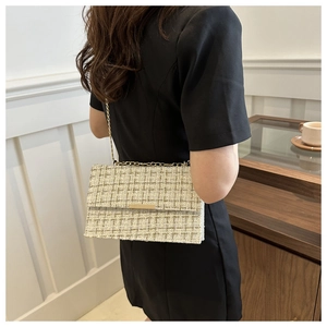 Detail of tweed crossbody bag with gold chain strap shown on model in a modern room
