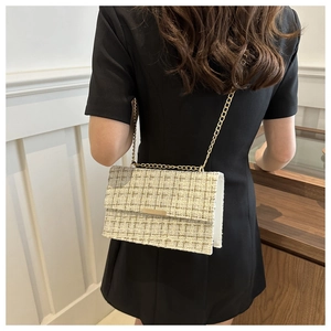 Detail of tweed crossbody bag with gold chain strap worn by a model in a black dress