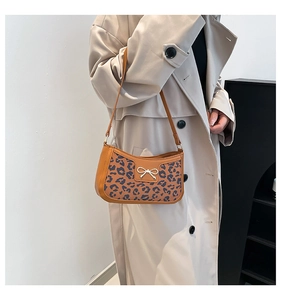 Detail of retro brown leather shoulder bag featuring leopard print and metal bow accent