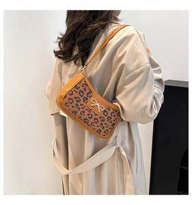 Leopard print underarm bag with silver bow detail shown on shoulder with brown leather trim