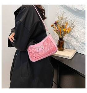Detailed view of pink crocodile pattern baguette bag featuring a metal bow accent