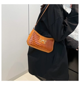 Detail of a brown crocodile pattern shoulder bag with a gold metal bow on black clothing