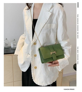 Detail of green crocodile embossed crossbody bag with gold chain and clasp on white suit