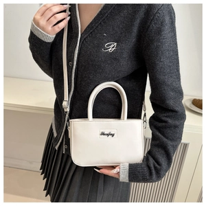 Detail of a creamy white leather mini handbag with silver logo plate and shoulder strap
