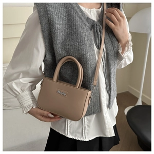 Detail of light brown leather crossbody bag with dual handles and metal logo plate