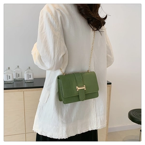 Detail of green crocodile textured crossbody bag with gold chain strap on model