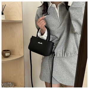 Detail of black mini tote bag in faux leather with logo shown in a lifestyle setting