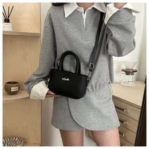 Detail of minimalist black matte leather mini crossbody bag with cylindrical top handles