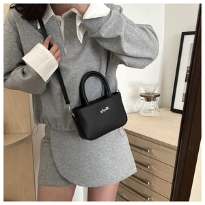 Dettaglio di una borsa minimalista in pelle nera con manico tondo e tracolla sottile