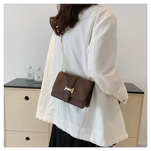 Detailed view of brown crocodile texture flap bag featuring a golden H-shaped clasp