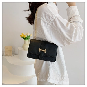 Close-up of black crocodile-embossed leather handbag featuring a gold H-buckle and chain