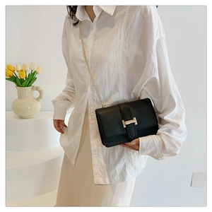 Detail of black croc-embossed crossbody bag with gold H-clasp on model in chic interior