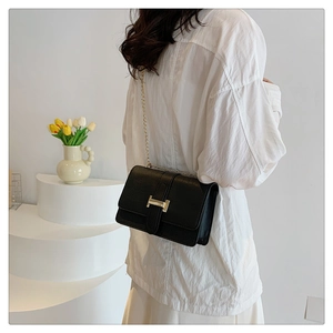 Close-up of black leather crossbody bag featuring a luxury gold H-shaped metal buckle