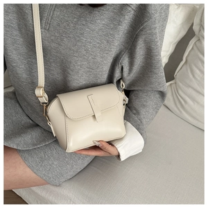 Detail of a creamy white PU leather crossbody bag with sleek vertical strap and gold buckle