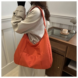 Detail of orange nylon tote bag with wide adjustable strap worn as a crossbody bag
