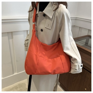 Detailed close-up of a large orange nylon crescent crossbody bag worn by a model