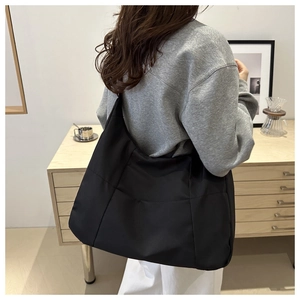 Side view of large black nylon tote bag worn by model in minimalist indoor home setting