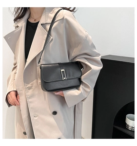 Detail der minimalistischen schwarzen Ledertasche mit Schnalle auf beigem Trenchcoat