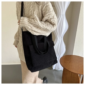 Detail of black corduroy tote bag featuring a large front pocket and adjustable strap