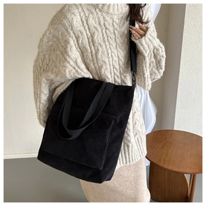 Large black corduroy tote bag with front pocket and adjustable strap worn by a model