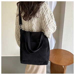 Detail of black corduroy tote bag with adjustable strap shown on model in cozy interior