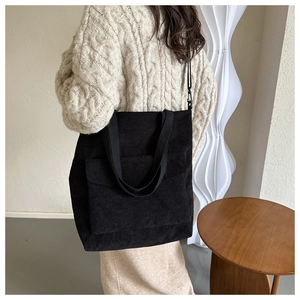 Close-up of black corduroy tote bag with front pocket, styled on a person in white sweater