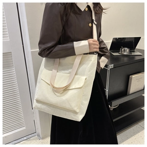 Detail of cream corduroy tote bag showing the texture, front pocket, and adjustable strap