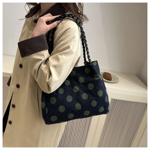 Detail view of navy blue knitted tote bag with green polka dots and woven black straps