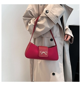 Detail of trendy magenta underarm bag with gold bow clasp on beige trench coat