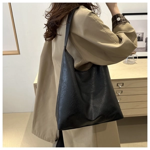 Side view of a large black vintage leather tote bag worn by a model in a minimalist room