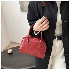 Detail of red leather Boston bag featuring embossed logo and premium double handles